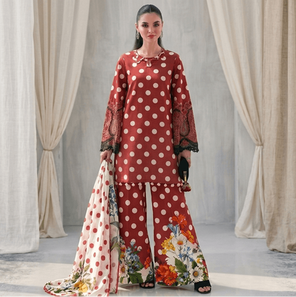 Woman in a red and white polka dot outfit with floral pants standing in front of draped curtains.