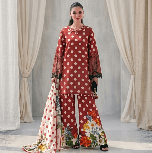 Woman in a red and white polka dot outfit with floral pants standing in front of draped curtains.